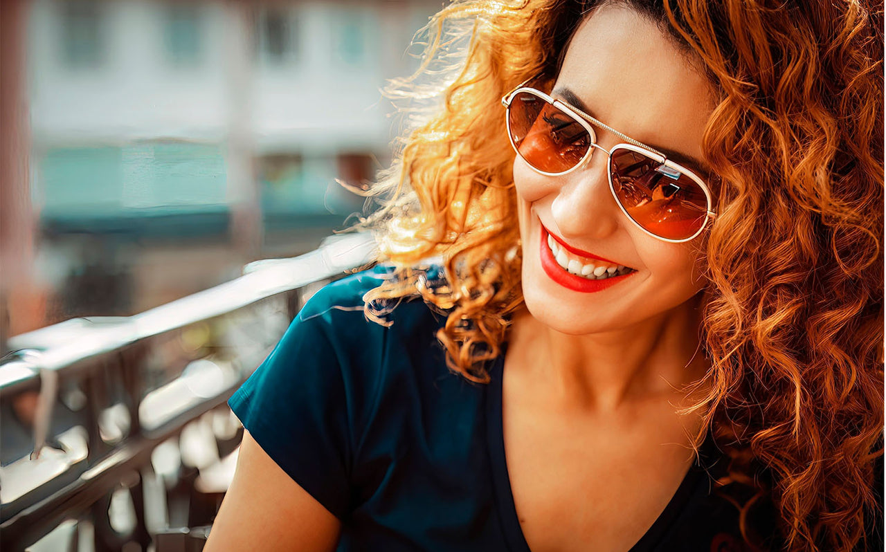 Smiling woman with vibrant curly red hair and sunglasses enjoying outdoor sunny day