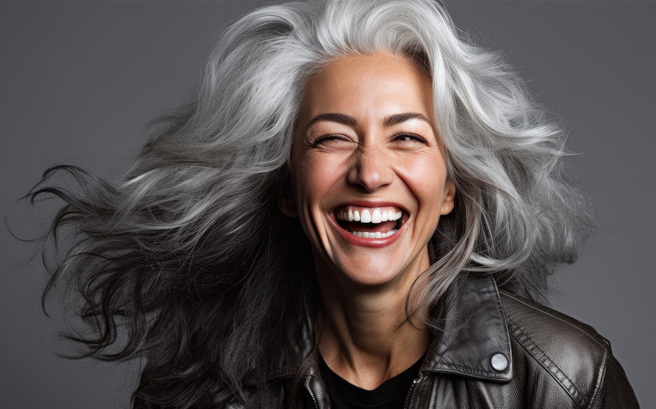 Happy mature woman with long flowing gray hair wearing a leather jacket against gray background