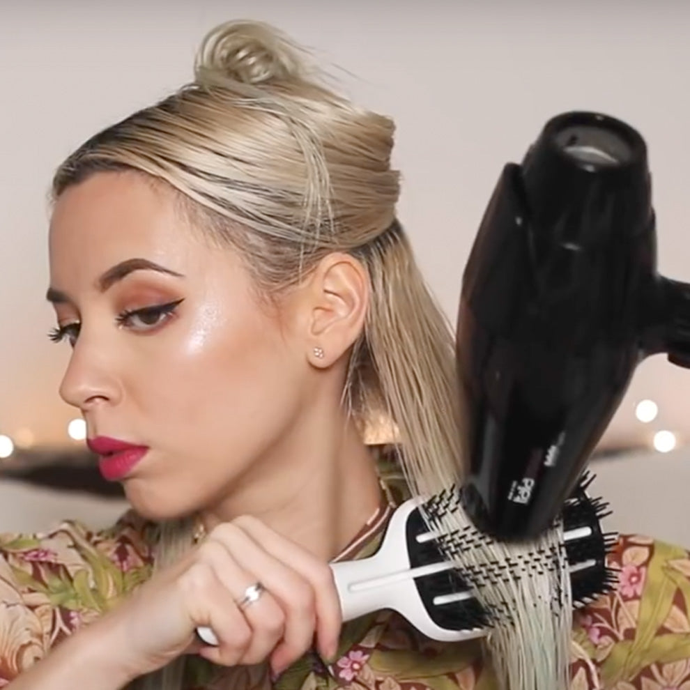 Woman with blonde hair blow drying and smoothing hair using round brush